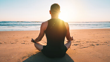 A man peacefully meditating on a beach at sunset, finding serenity amidst the tranquil beauty of nature.